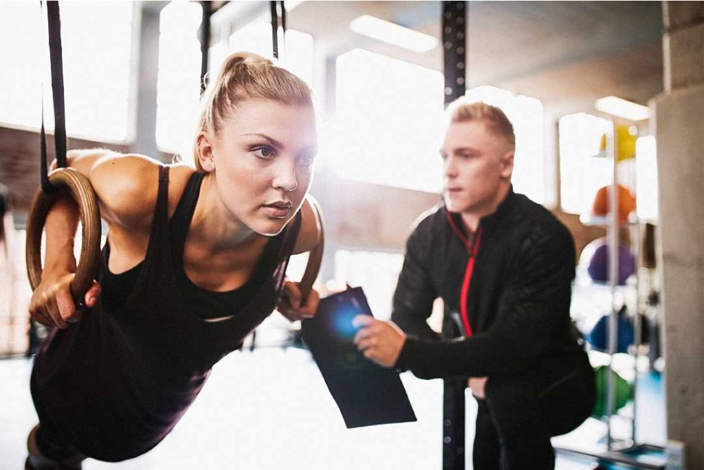 A personal trainer checks a woman while she is performing a ring push up