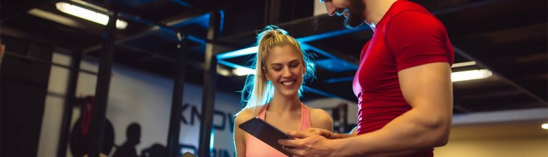 a man shows to a woman a workout program on tablet in a calisthenics gym